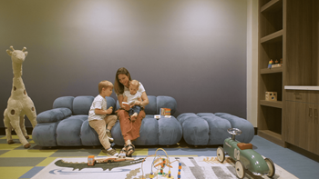A woman and two children are sitting on a blue couch in a room with a wooden floor and a grey wall.